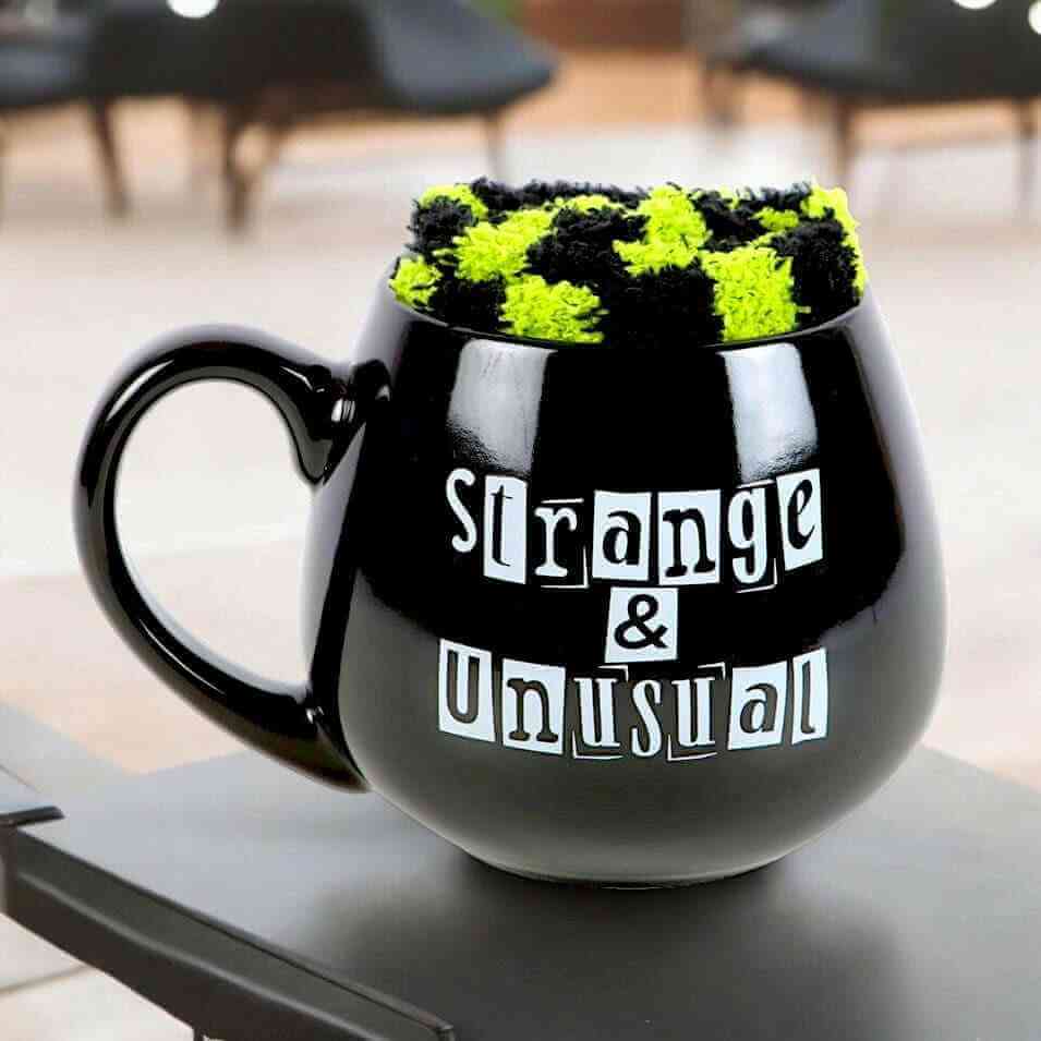 Black novelty mug with green fuzzy top and 'Strange & Unusual' print
