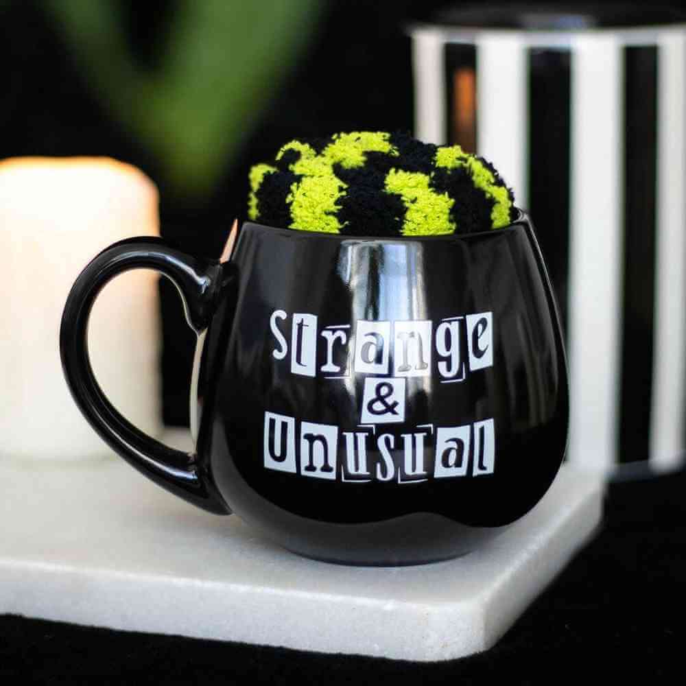 Black novelty mug with green fuzzy top and 'Strange & Unusual' print on base