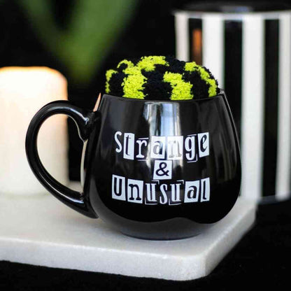Black novelty mug with green fuzzy top and 'Strange & Unusual' print on base