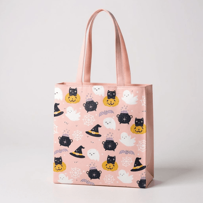 Pink Halloween tote bag with ghost, pumpkin, and cat faces print; front view handles