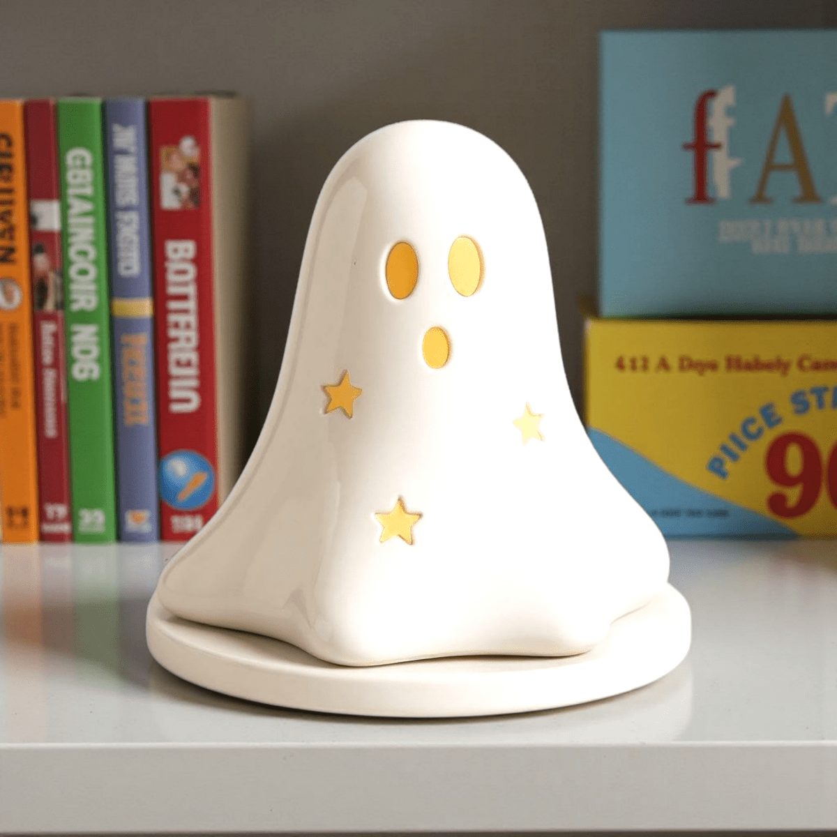 White ceramic ghost tealight holder with painted orange eyes, gold stars, and round base