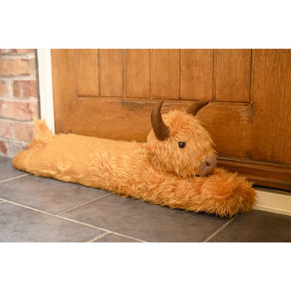 Orange plush Highland cow draught excluder lying on floor tiles, head facing forward.