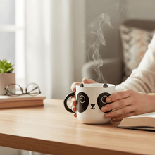 White panda mug with steam rising while hands hold it; black handle and face