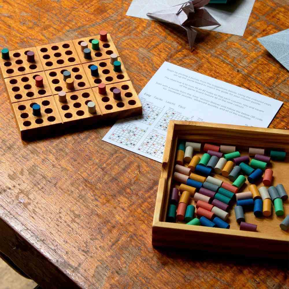 Wooden colour sudoku board with colored pegs, papers, and open wooden compartment