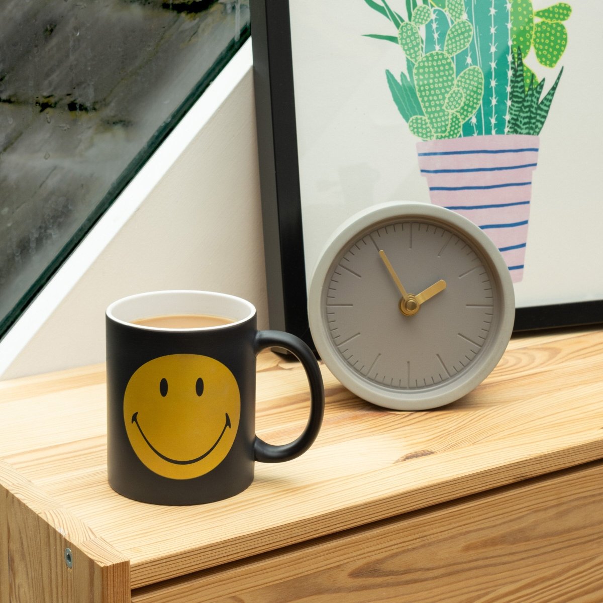 Black mug with yellow smiley face graphic, with tea cup beside it
