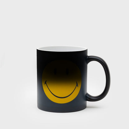 Black ceramic mug with yellow smiley face graphic visible on the front