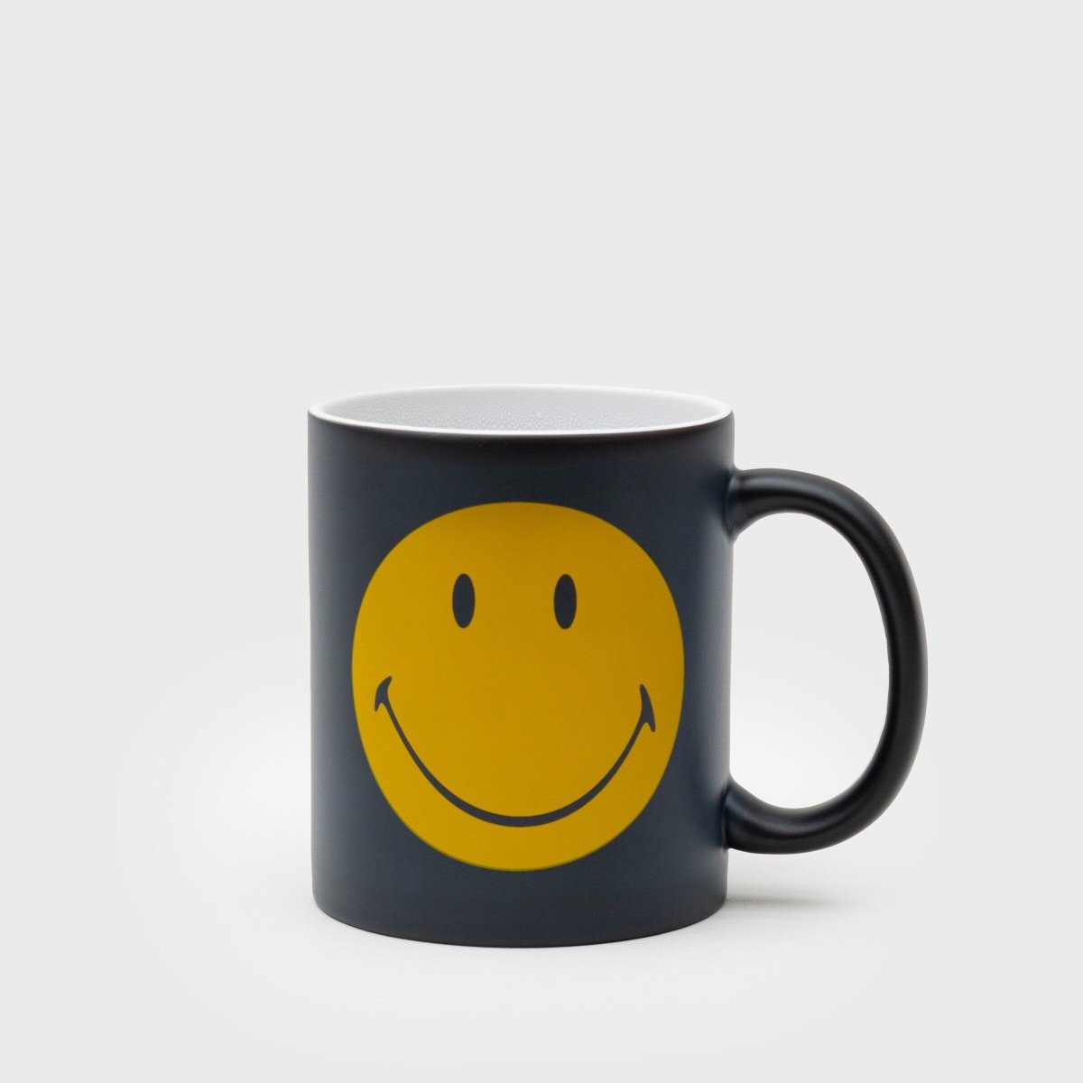 Black ceramic mug with yellow smiley face graphic and curved handle