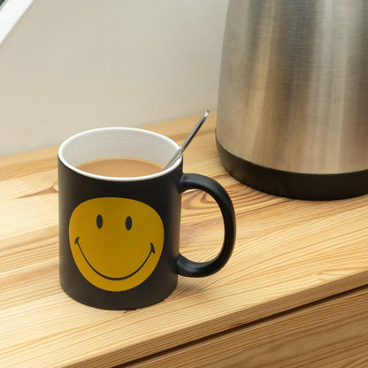 Black mug with yellow smiling face, heat-sensitive design, curved handle