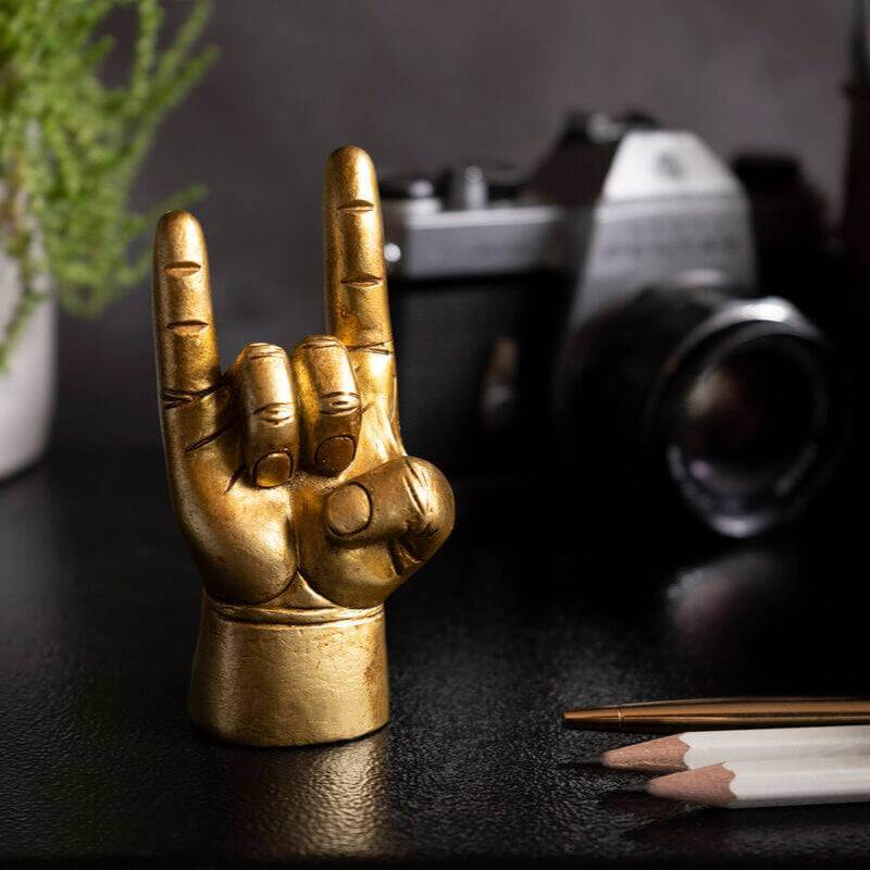 Gold rock-on hand ring holder statue on desk with pencil nearby