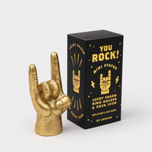 Gold metal ring holder shaped like a rock-on hand, beside black mini statue box