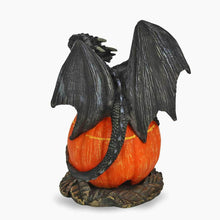 Black dragon cone burner figurine holding orange carved jack-o’-lantern, side view