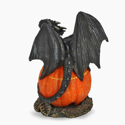 Black dragon cone burner figurine holding orange carved jack-o’-lantern, side view