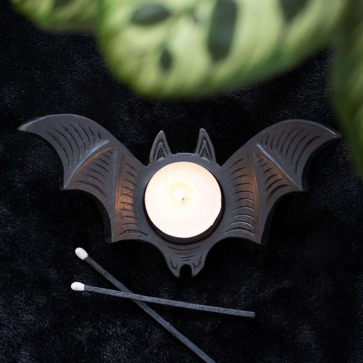 Bat-shaped tealight candle holder with lit white candle in round opening, black.