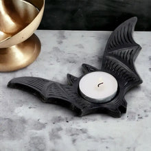 Black bat-shaped tealight candle holder with lit white candle centered in round cup.