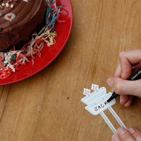 Hand holding cake topper sticks with 'JACK' text and star cutout decorations