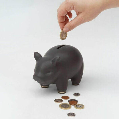 Black piggy bank as a hand drops a coin, with scattered coins beside it