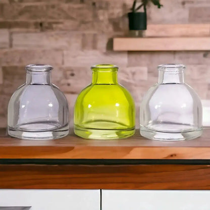 Three mini glass bud vases with rounded bodies in smoky grey, lime green, clear.