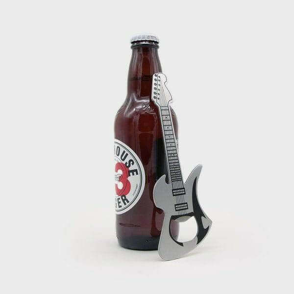 Guitar-shaped stainless steel bottle opener beside a brown beer bottle.
