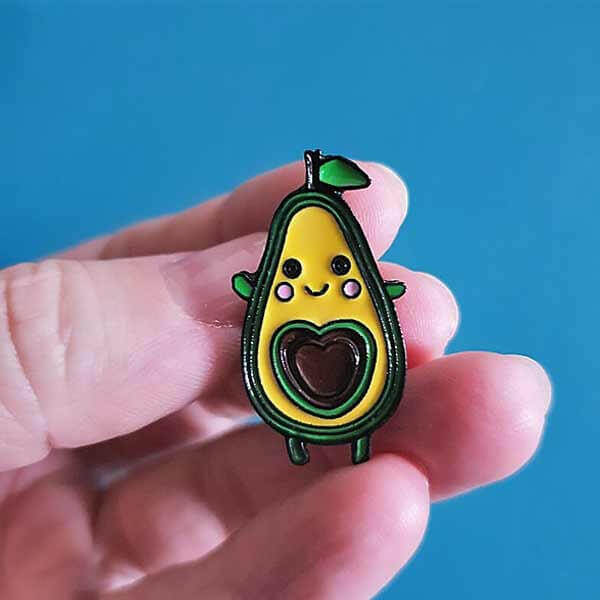 Avocado enamel pin badge with smiling face and dark heart belly, green and yellow