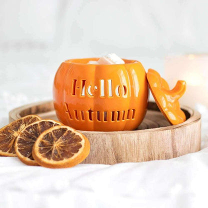 Orange pumpkin wax melt burner with carved text, open lid, wood tray and citrus slices