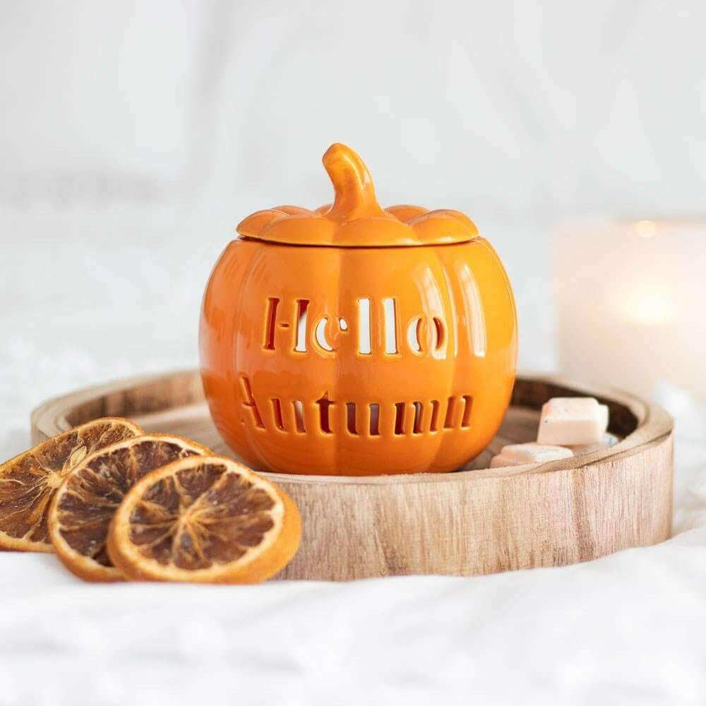 Orange pumpkin wax melt oil burner with carved lid on round wood tray, citrus slices