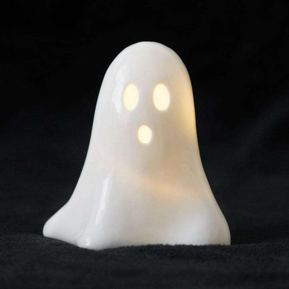 White ceramic ghost LED night light with glowing eyes, lit, front view.
