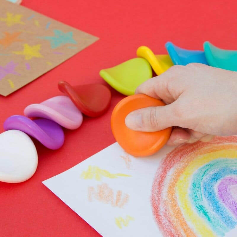 Jumbo grip crayons held in a hand, with bright orange, yellow, green, and blue tips.