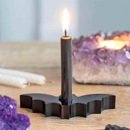 Flame-lit black pillar candle in a stepped holder on wooden surface
