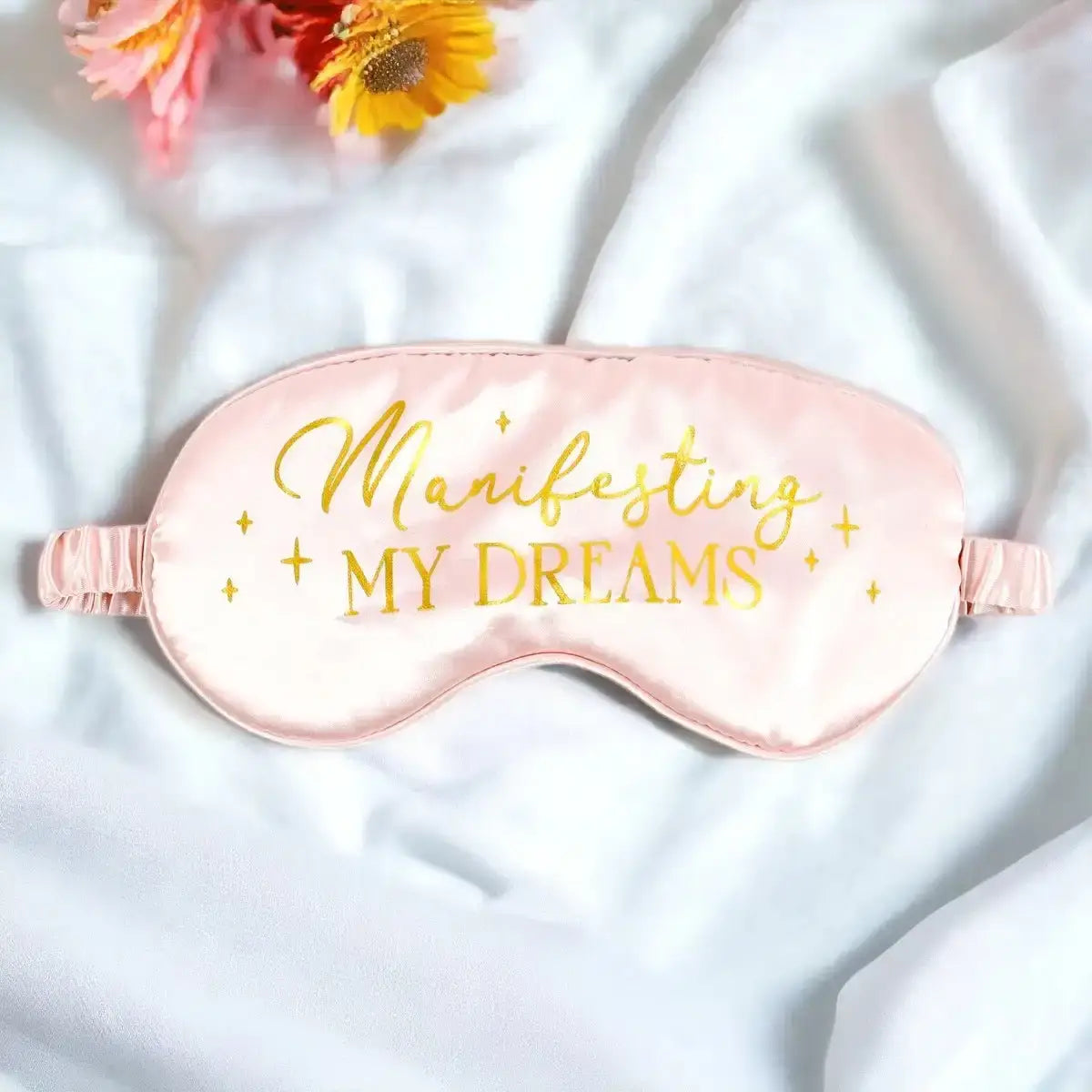Satin sleep eye mask in blush pink with “Manifesting My Dreams” gold lettering