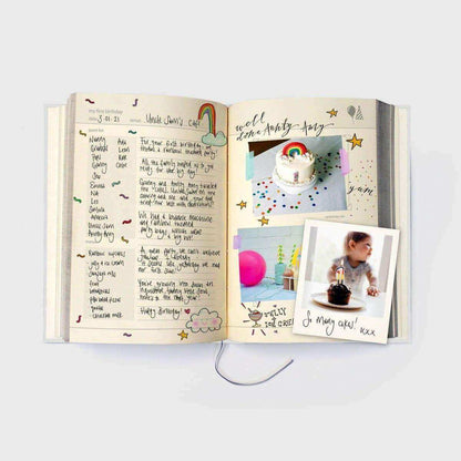 Baby years journal open to handwritten-style pages with baby photo and decorated cake image