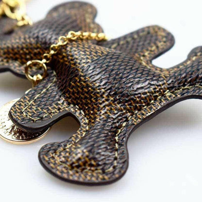 Close-up patchwork teddy bear keyring with woven dark brown texture and gold chain