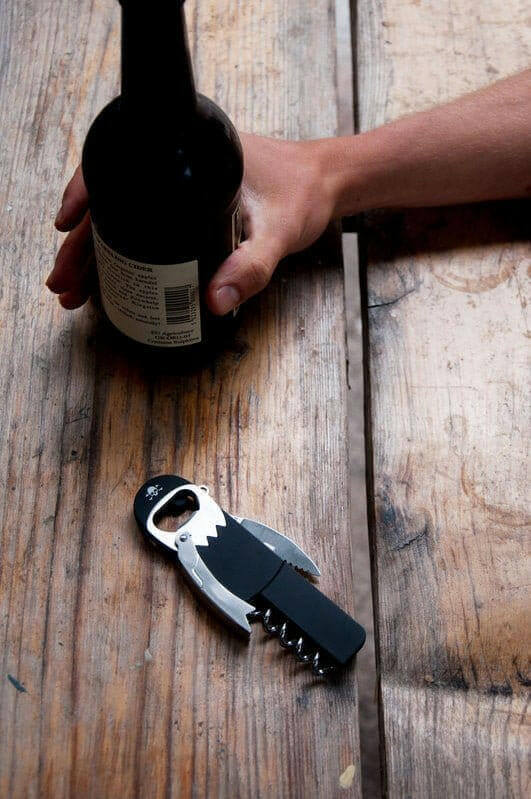 Pirate waiter’s friend corkscrew and bottle opener tool with black handle near bottle.