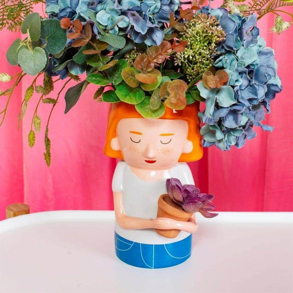 Plant mum planter with orange hair, holding a small purple flower cluster in blue pot