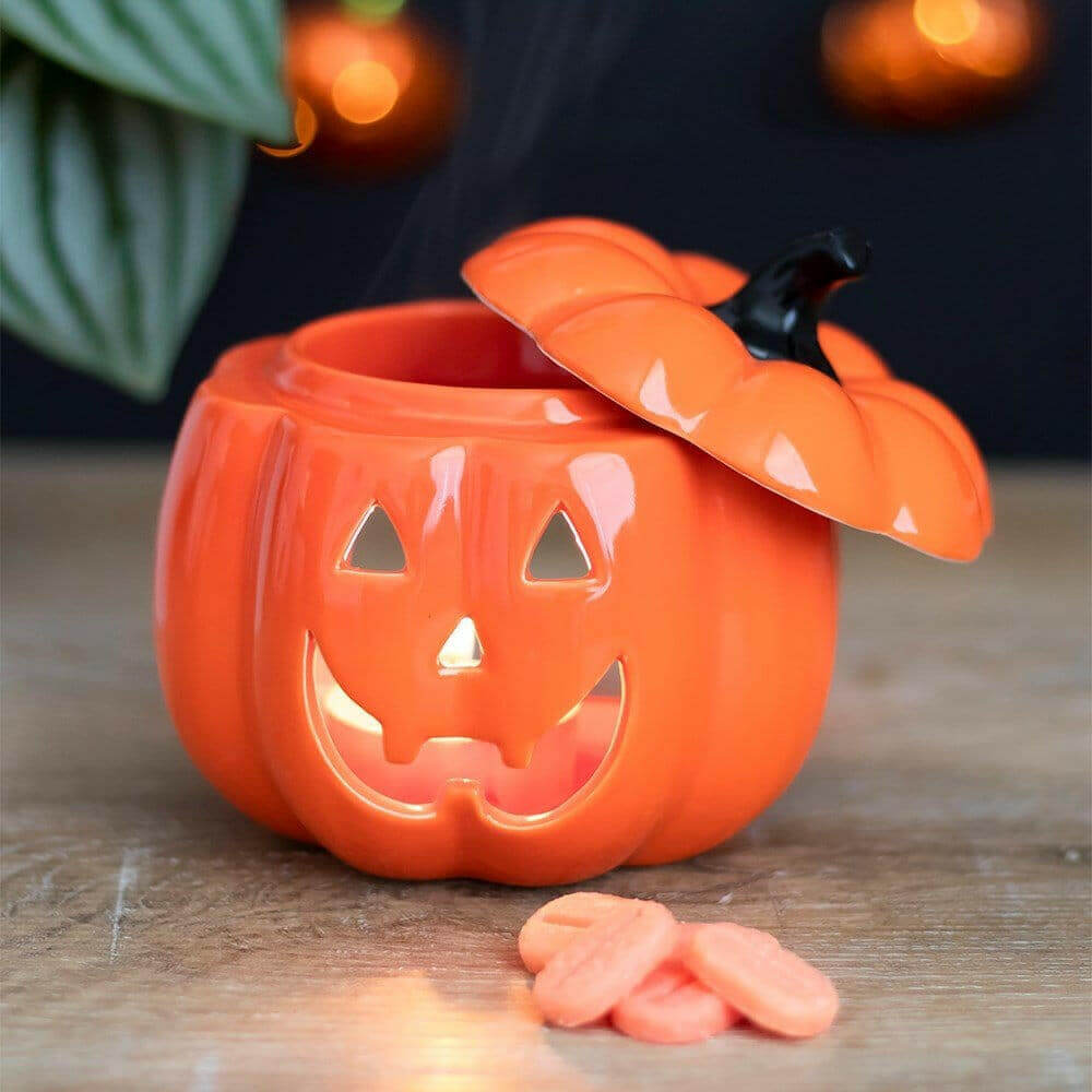 Orange jack-o-lantern oil burner with lit face and wax melt pieces nearby