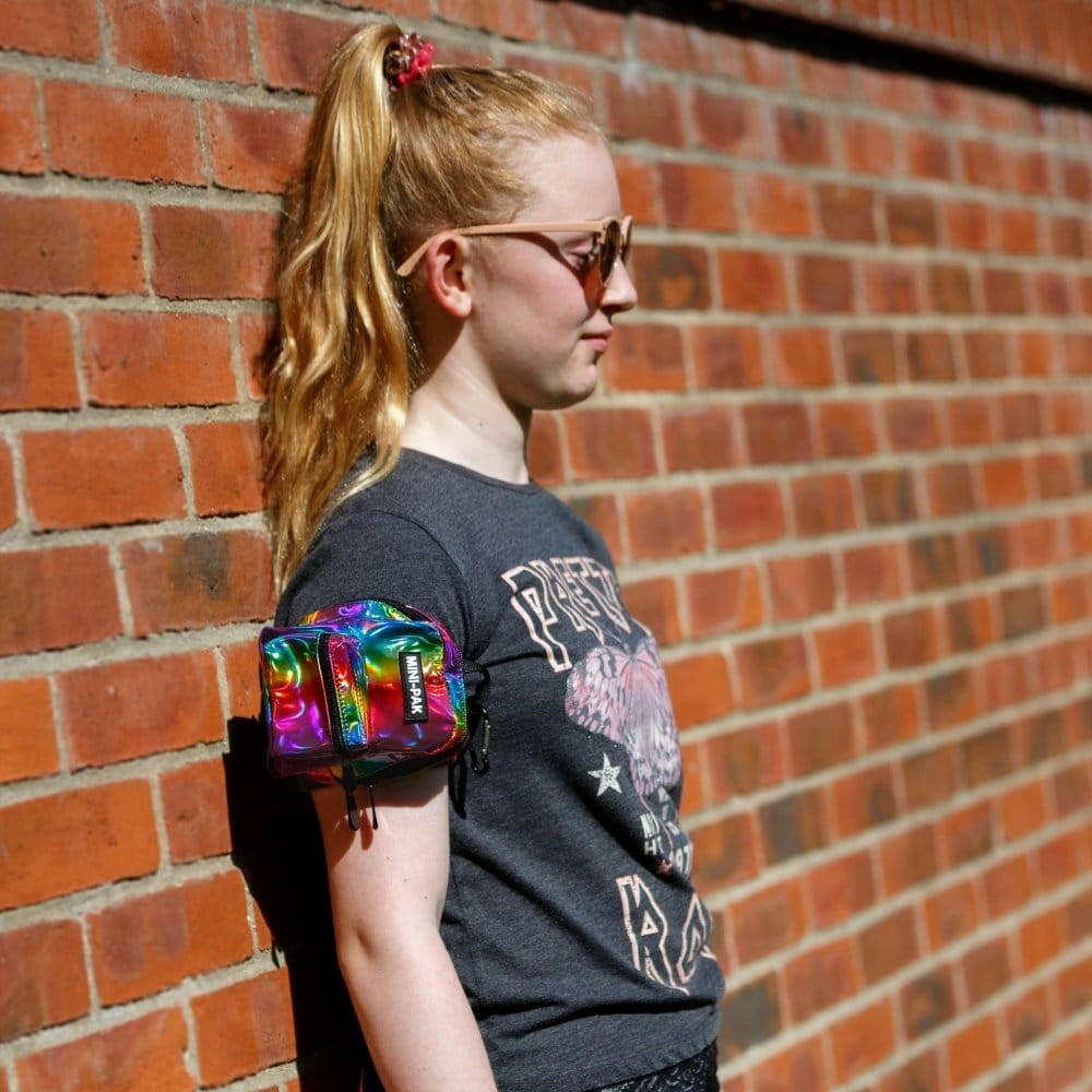 Rainbow metallic mini backpack worn cross-body with front zip pocket and black straps.