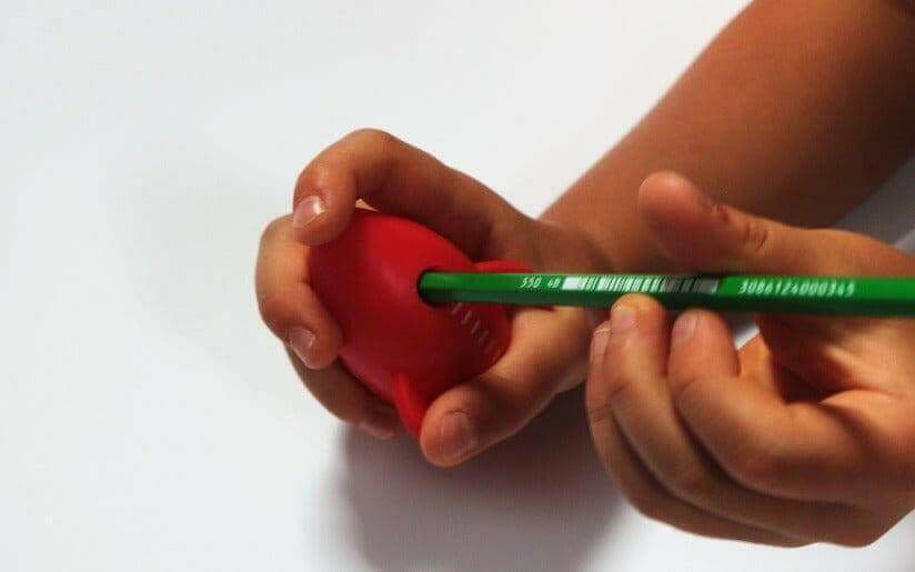 Hands holding a pencil to a red rocket pencil sharpener for sharpening.
