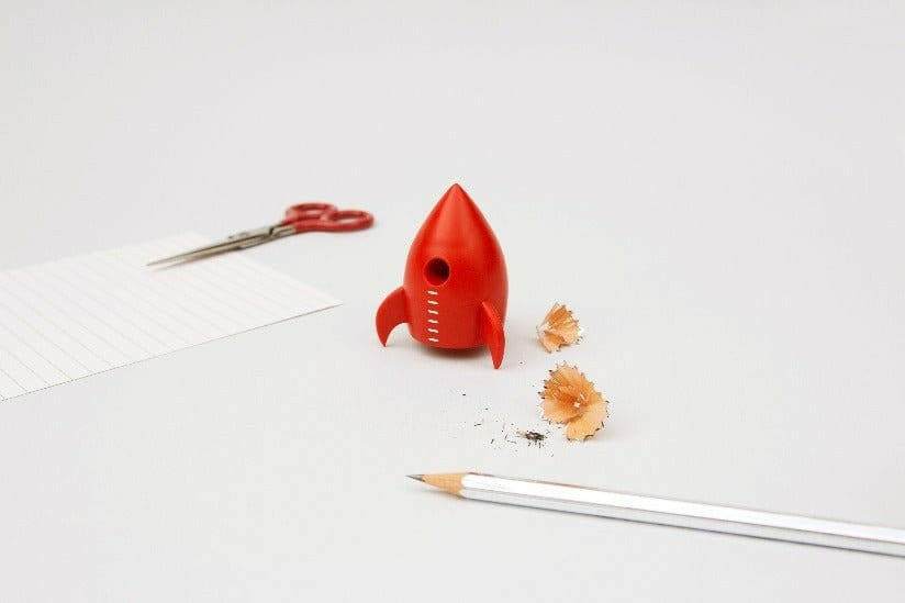 Red rocket pencil sharpener on a notebook with pencil and wood shavings scattered around.