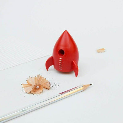 Red rocket pencil sharpener with pencil and scattered wood shavings from the sharpening hole.