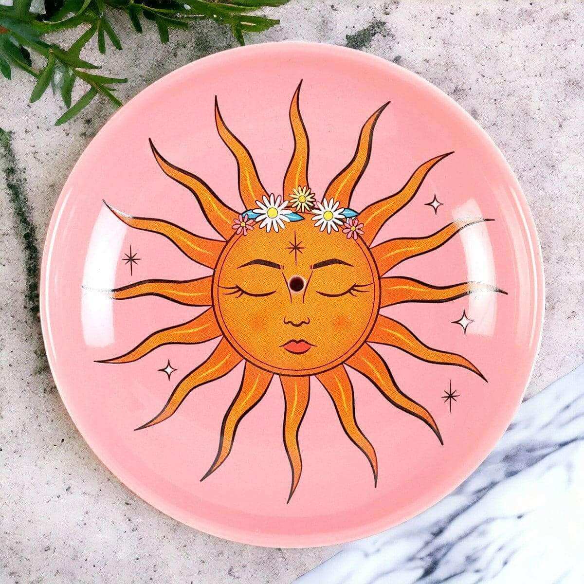 Pink circular incense holder with detailed sun face design and small flowers